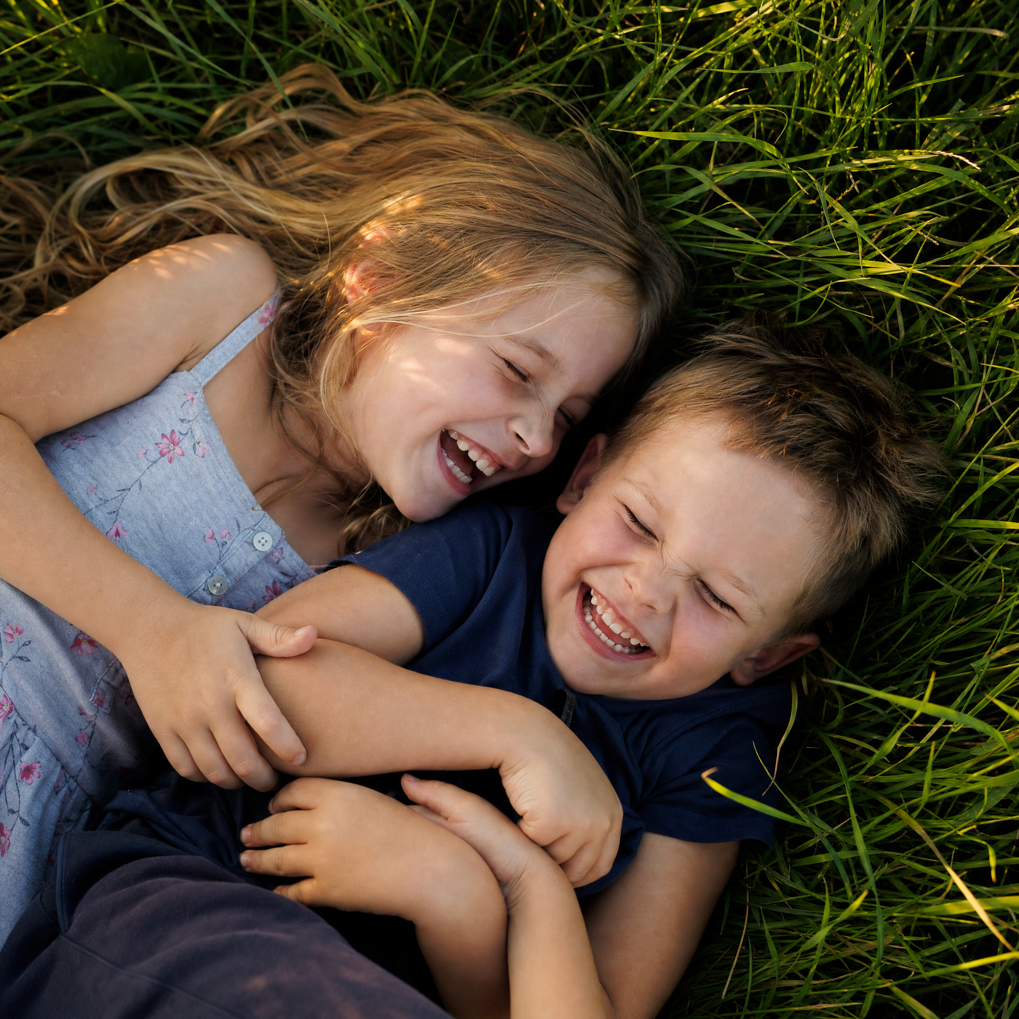 Siblings laughing together in the grass